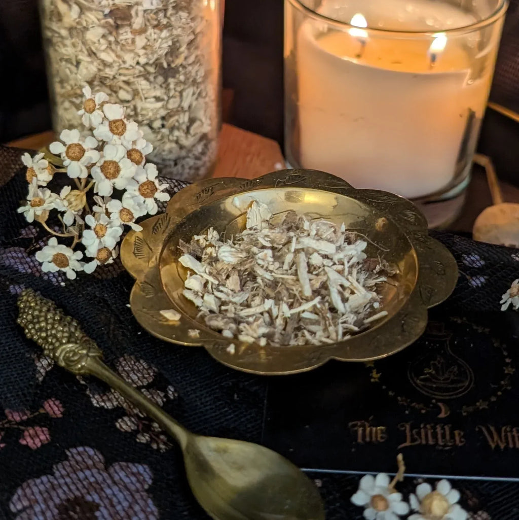 Gold bowl with dried Marshmallow Root herbs on a dark surface with flowers and a candle