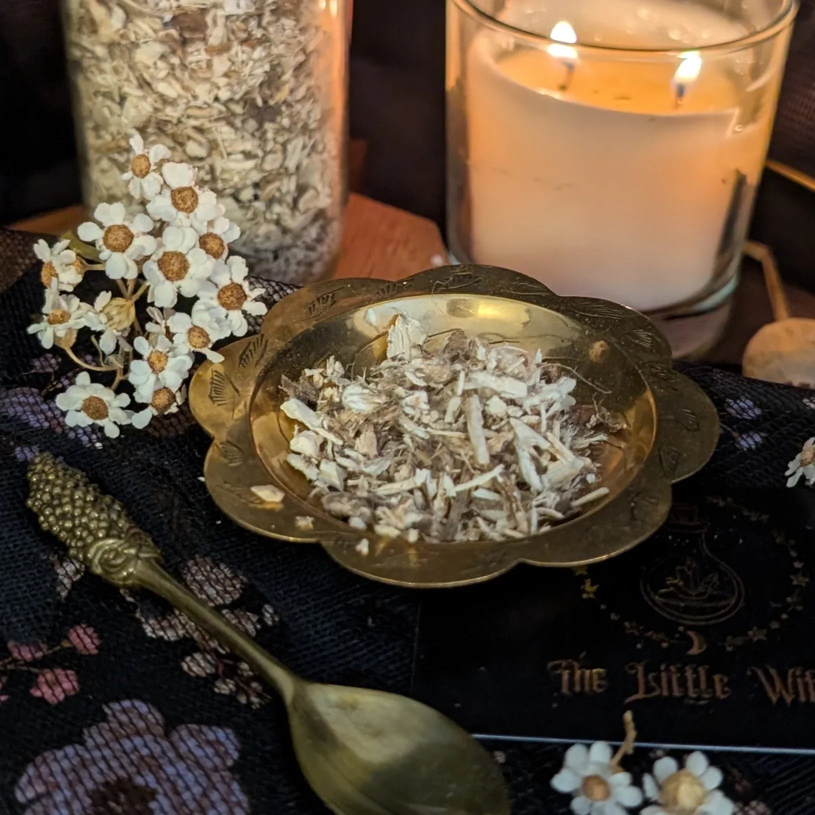 Gold bowl with dried Marshmallow Root herbs on a dark surface with flowers and a candle