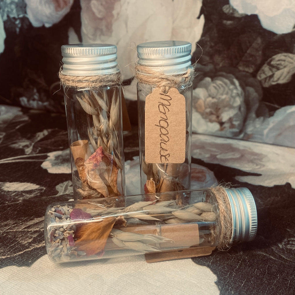 A plastic tube with screw top holding a variety of preserved flower, herbs and foliage along with a scroll of affirmation 