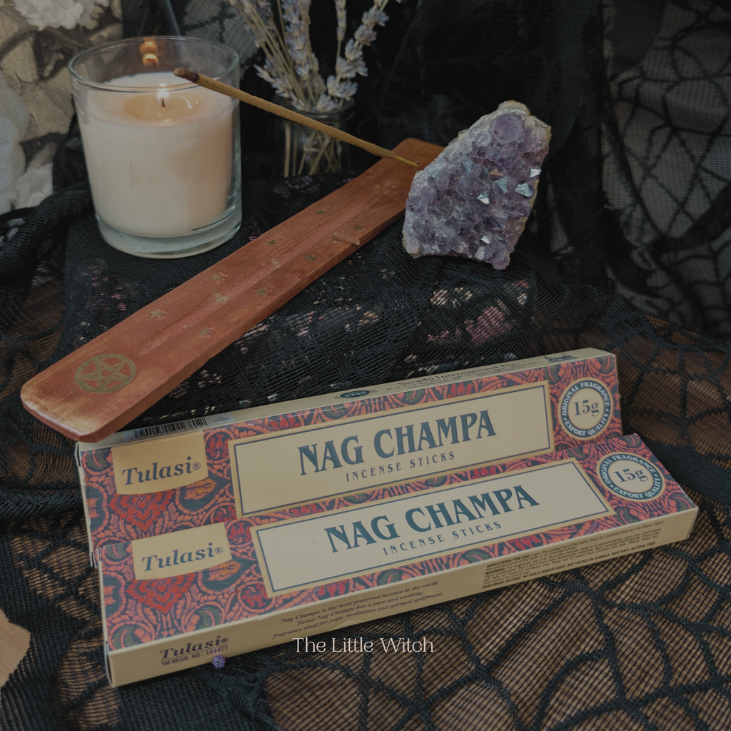 Box of Nag Champa incense sticks with a lit candle and amethyst crystal on a dark surface.