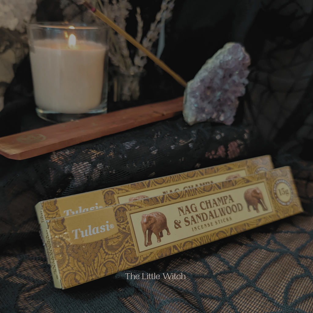 Nag Champa & Sandalwood incense sticks with a candle and crystal on a dark surface