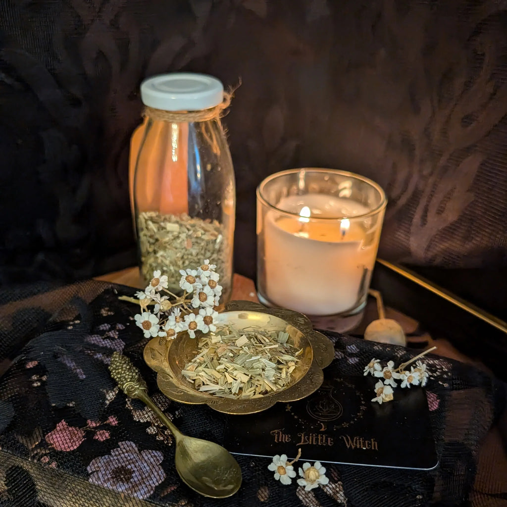 Decorative setup with a lit candle, glass bottle, and small bowl on a dark surface.
