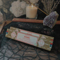 Box of Oodh incense with a lit candle and crystals on a dark fabric background