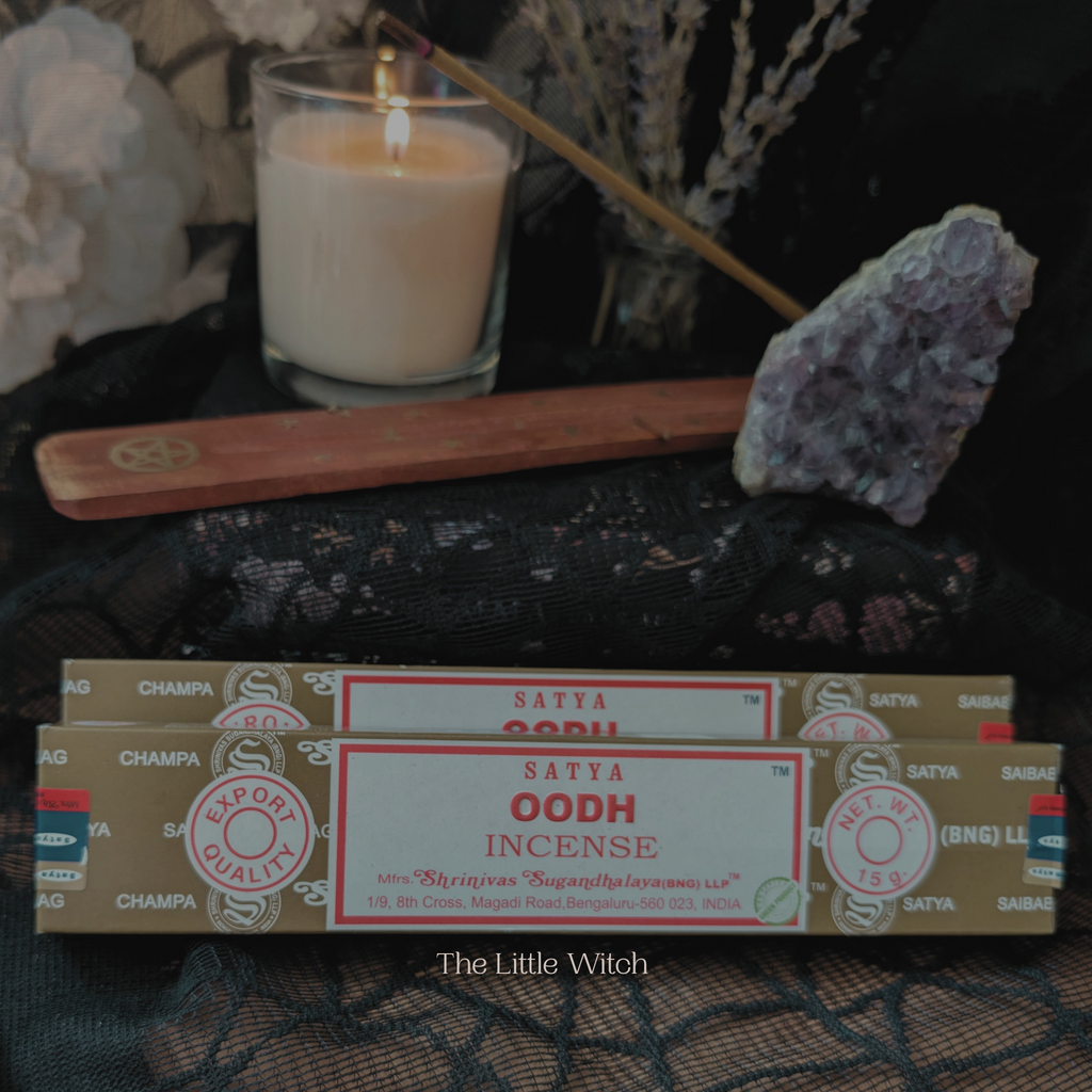 Oodh incense with a lit candle and wooden stick on a textured surface.