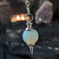 Opalite cone pendulum in the forefront with a black lace background