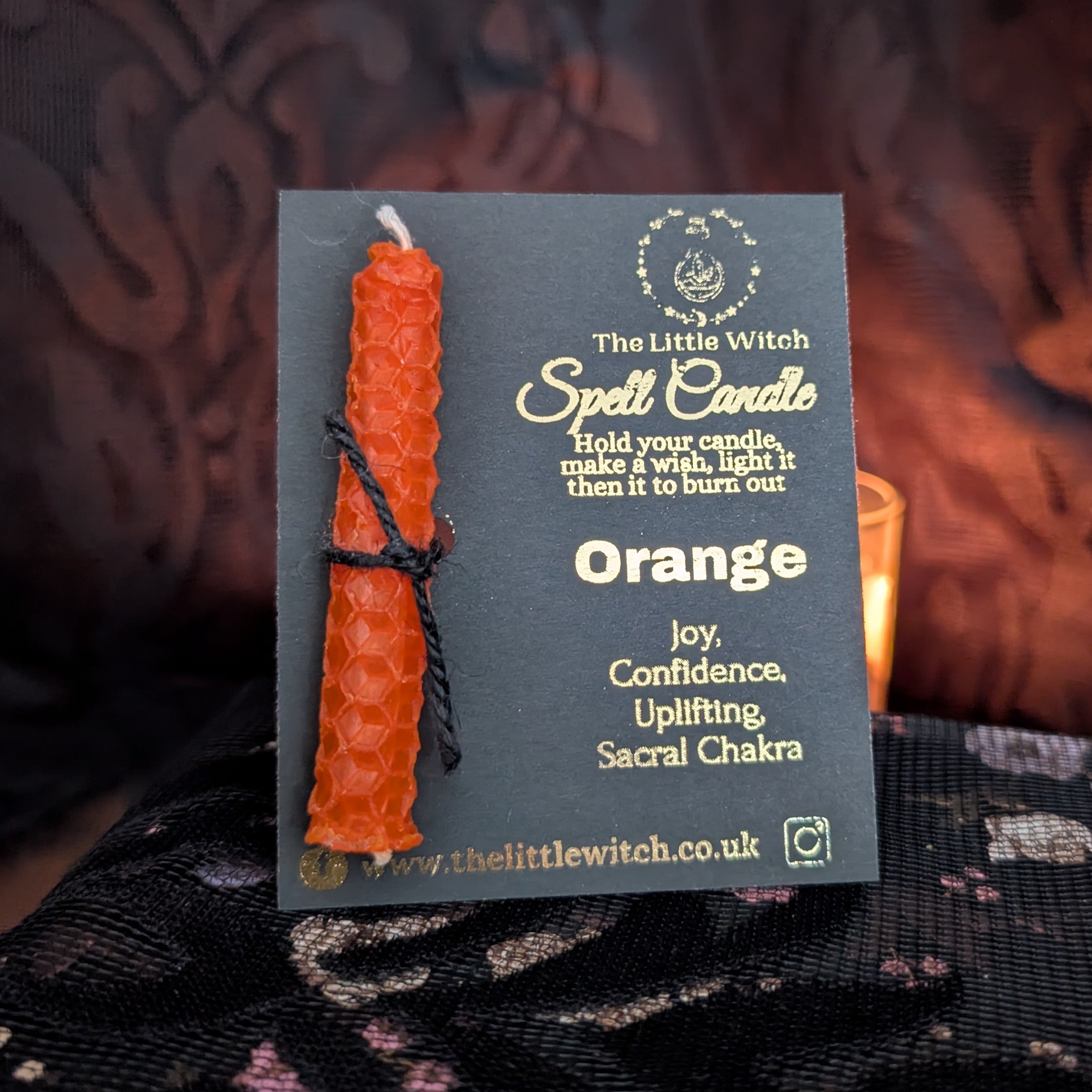 Orange spell candle with black and gold The Little Witch branding on a dark background