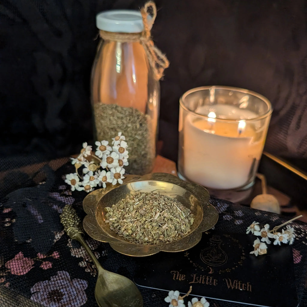 Dried Oregano in a bottle and bowl with a lit candle on a dark surface.