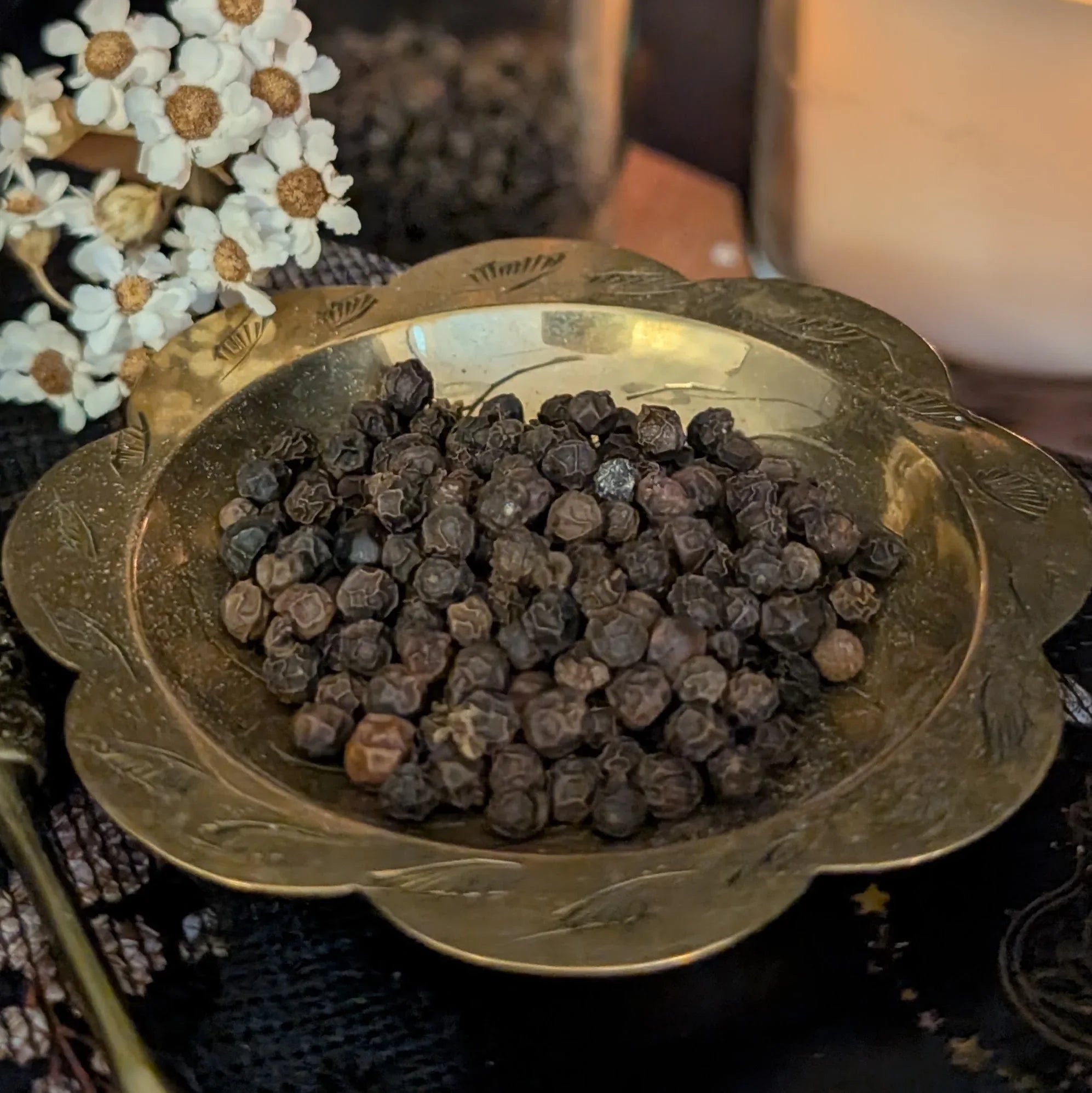 Black peppercorns in a decorative brass bowl with flowers in the background