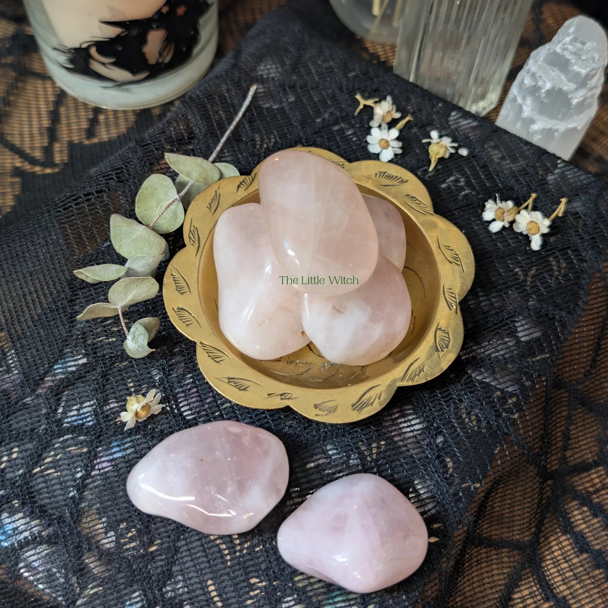 rose quartz in a gold dish on a textured surface with flowers and crystals.