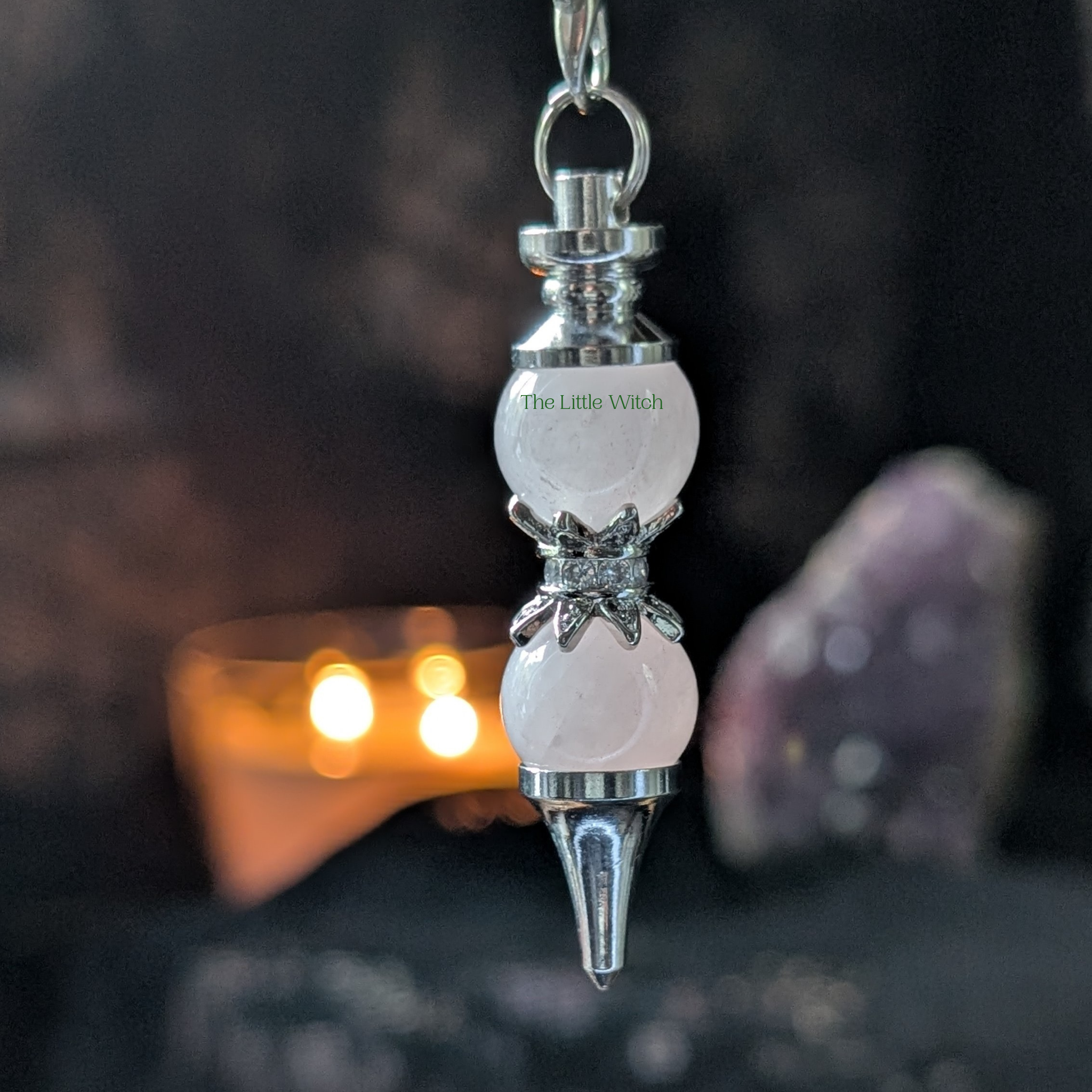 Rose Quartz double ball pendulum with 'The Little Witch' branding against a dark background with soft candle light and sparkling ameythst geode