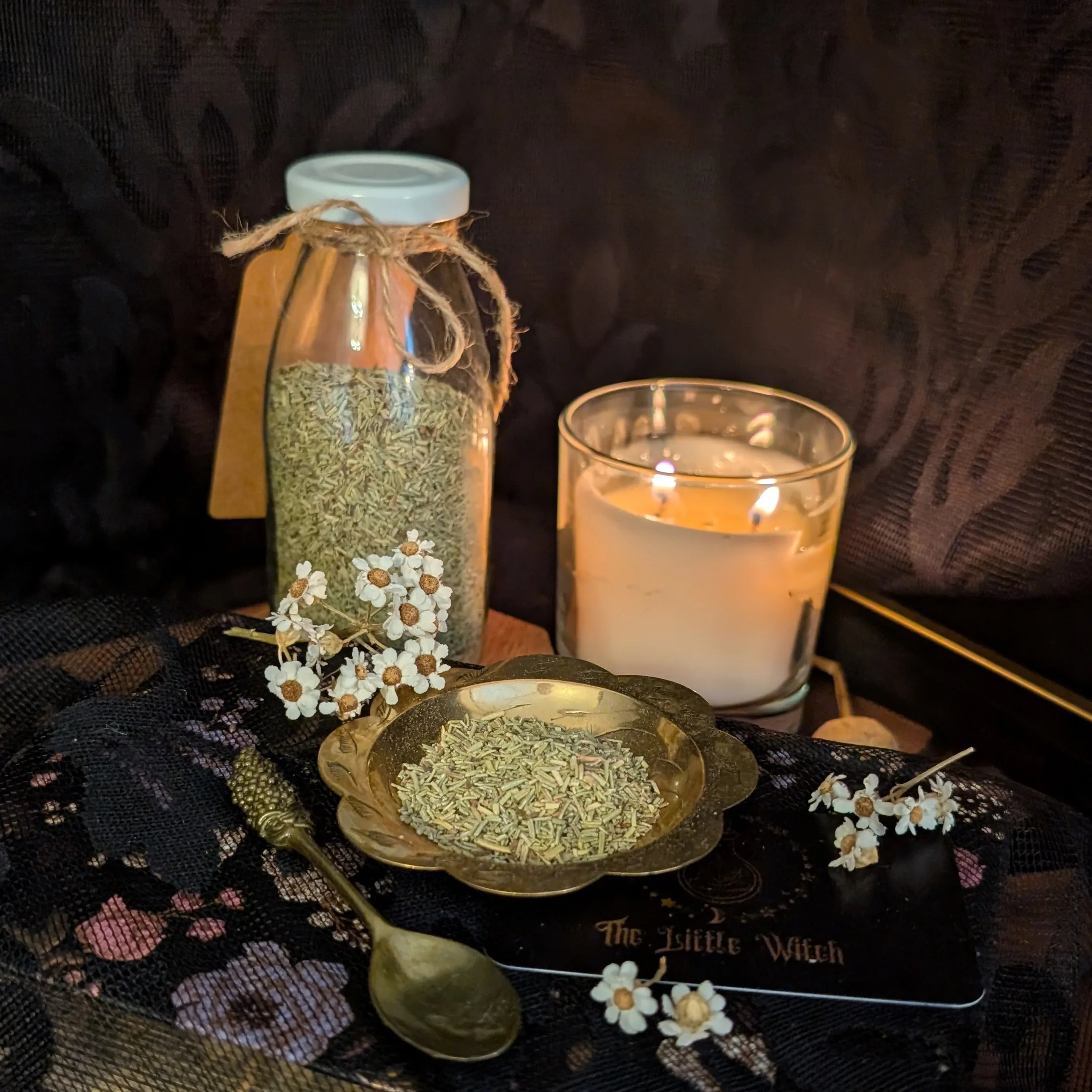 Dried Rosemary in a jar, on a dish, and in a glass with a lit candle on a dark surface.