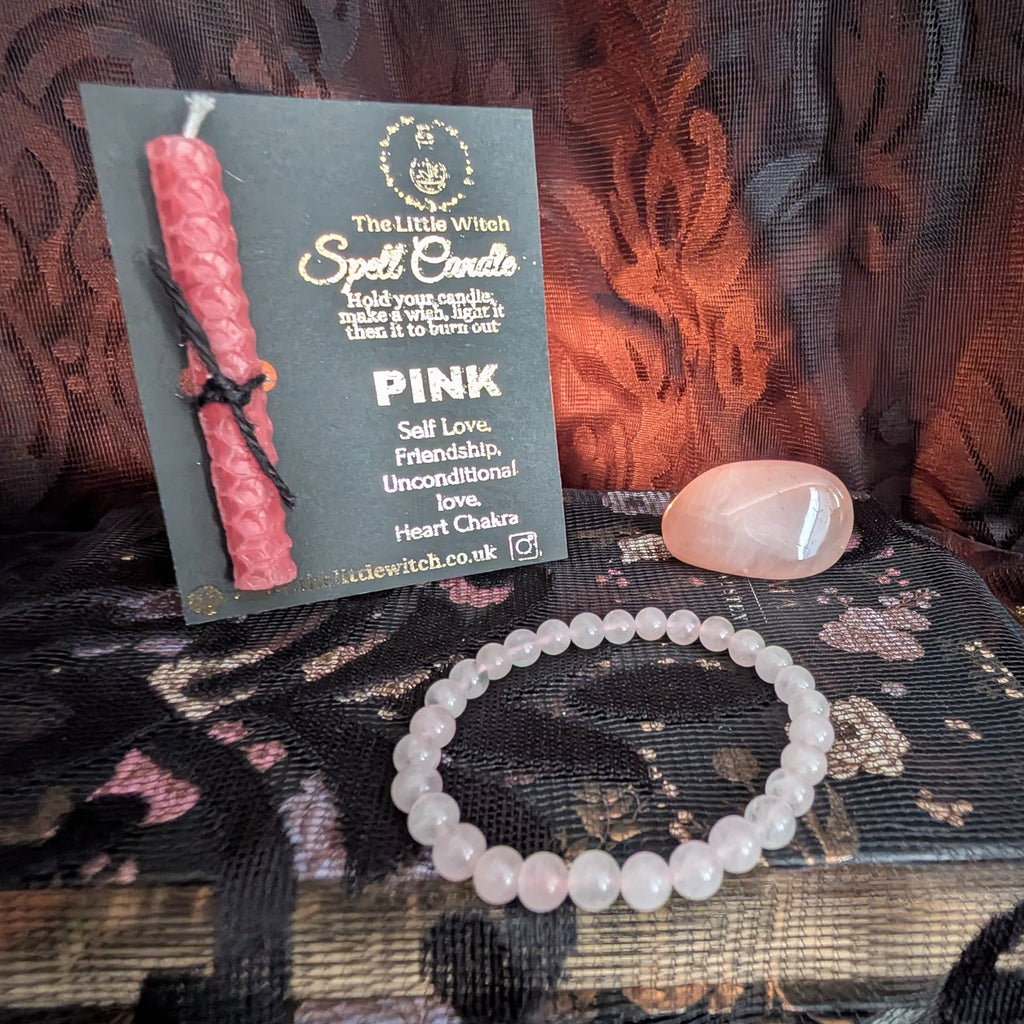 Pink candle, bracelet, and card on a textured surface