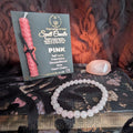 Pink candle, bracelet, and card on a textured surface