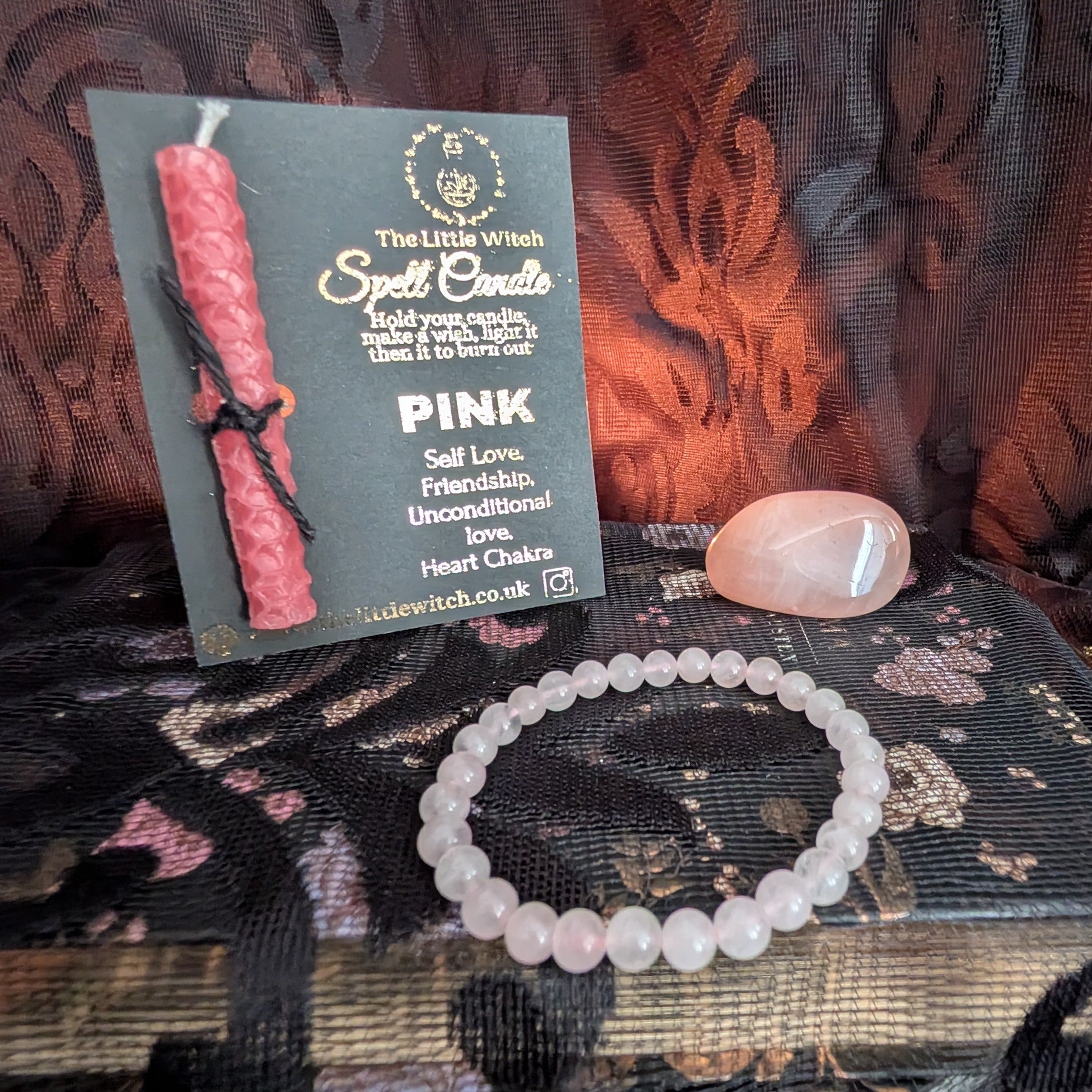 Pink candle, bracelet, and card on a textured surface