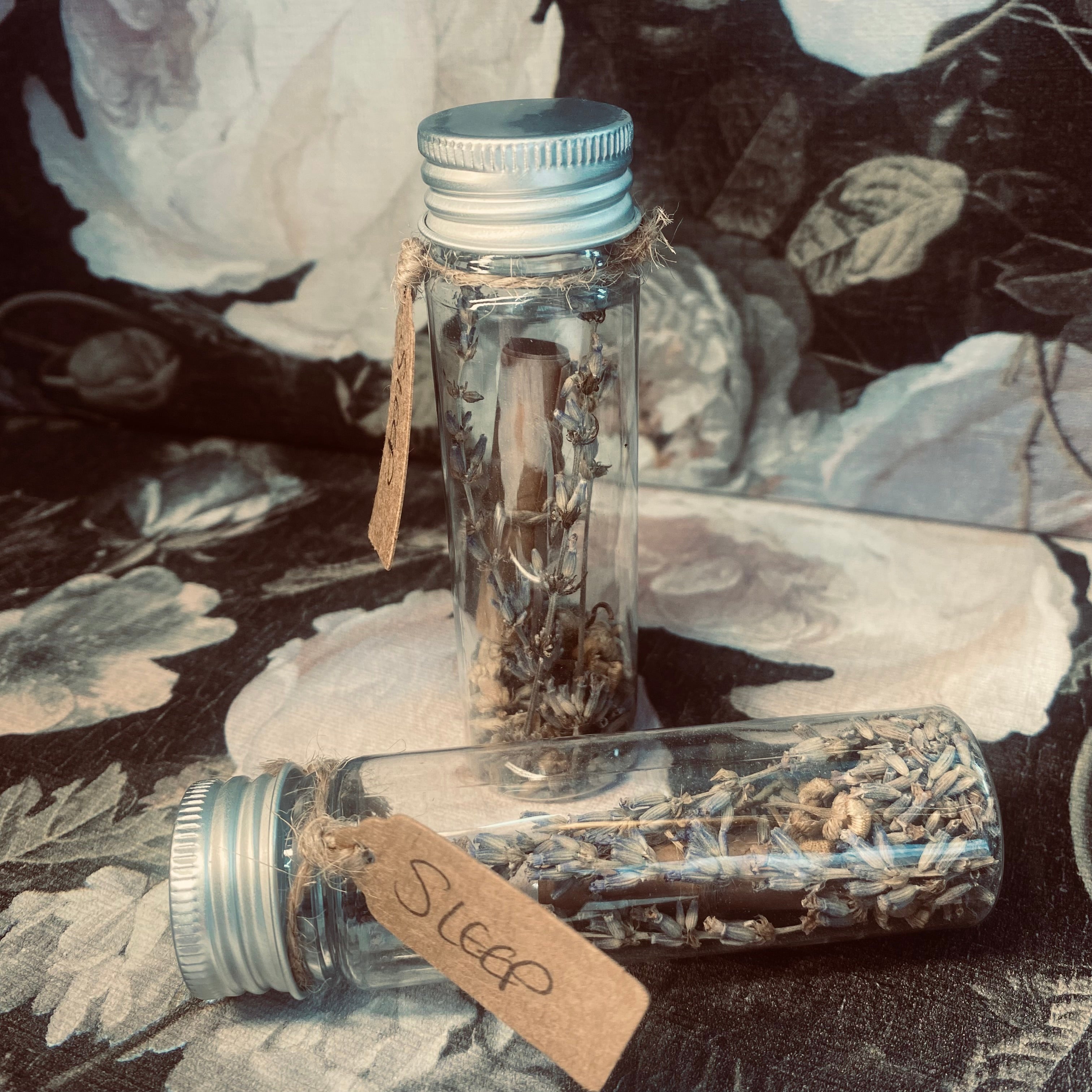 A screw top tube holding a variety of preserved flowers and herbs along with a handwritten scroll with the intention of a restful sleep.