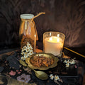 Candlelit scene with star anise, flowers, and a bottle on a dark fabric background.