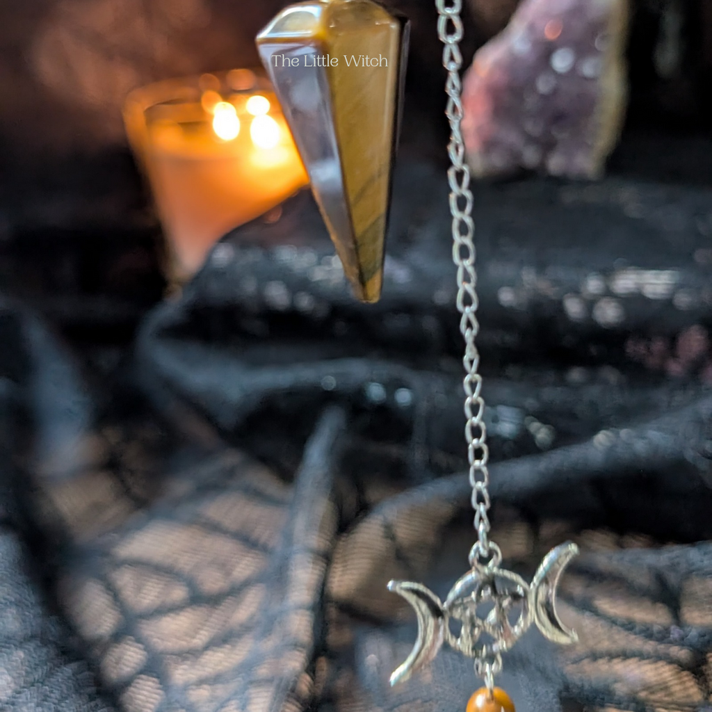 Tigers eye pendulum with triple moon adornment with a black lace background and soft candlelight
