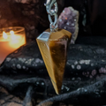 Tiger eye pendulum on a dark fabric background with a lit candle