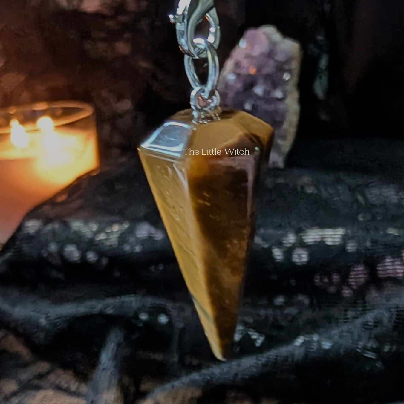 Tiger eye pendulum on a dark fabric background with a lit candle