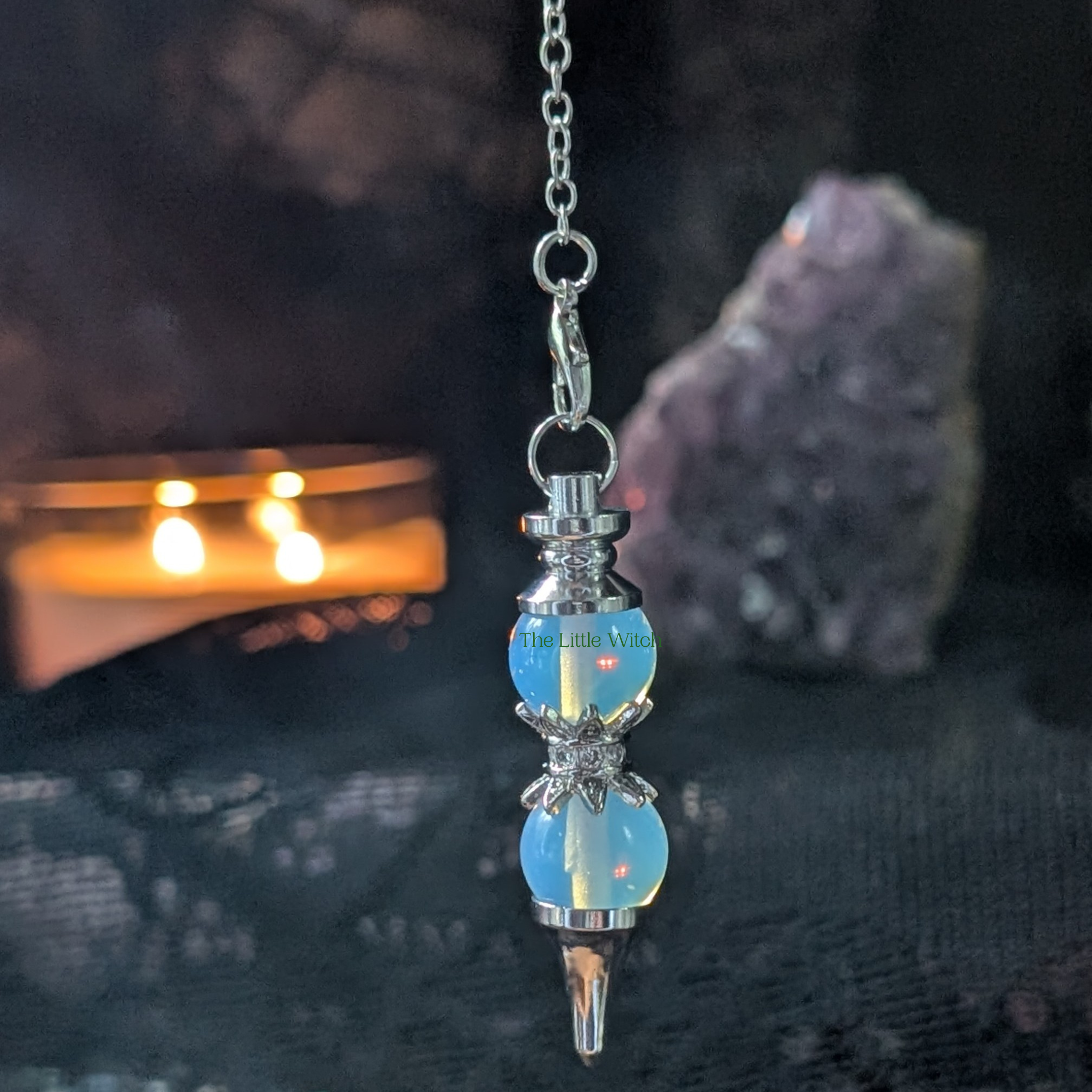 Double Opalite pendulum with black lace backdrop and a lit candle and amethyst geode in the background 