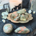 Unakite stones on a decorative plate with a black lace tablecloth and white flowers.