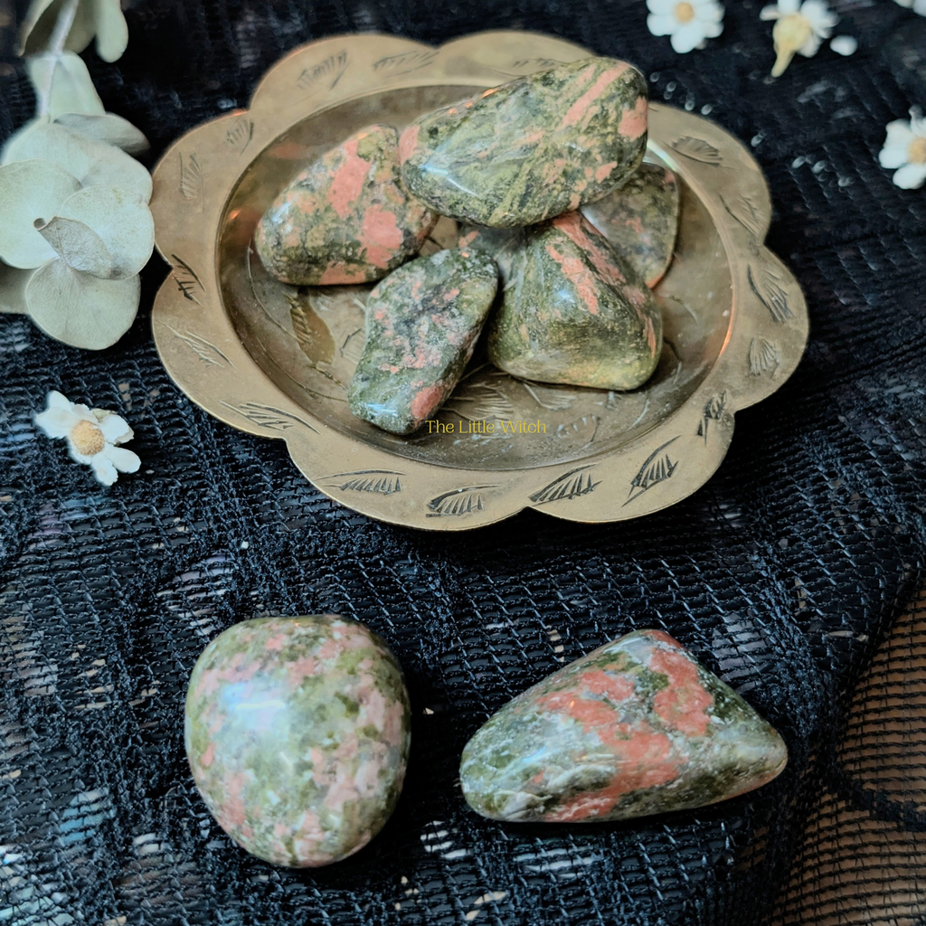 Unakite stones on a decorative plate with flowers on a textured black background
