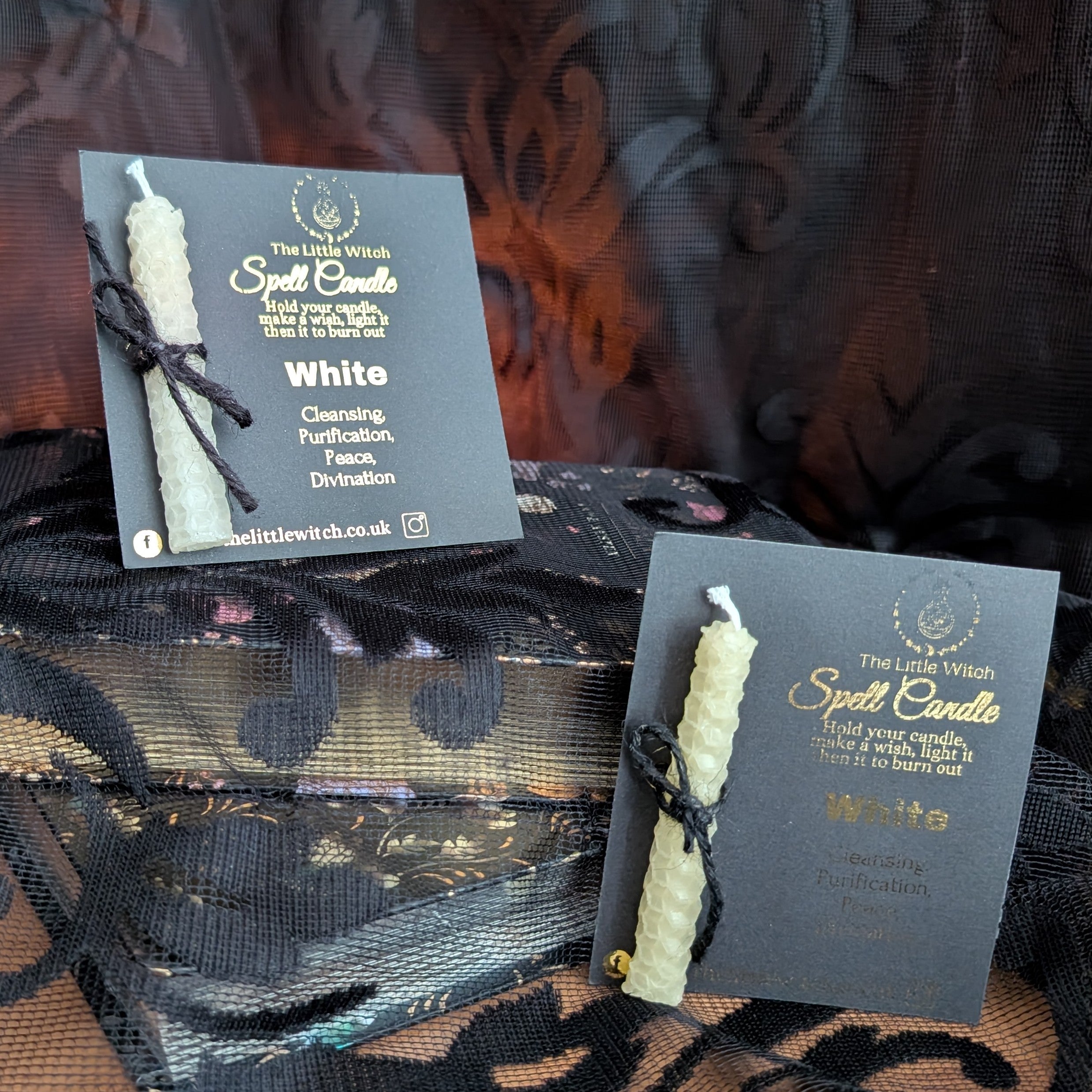 Two white spell candles with 'The Little Witch' branding on a dark textured background