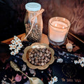 A gold bowl of whole Allspice with a lit candle and preserved flowers