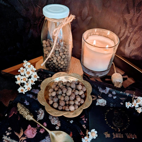 A gold bowl of whole Allspice with a lit candle and preserved flowers