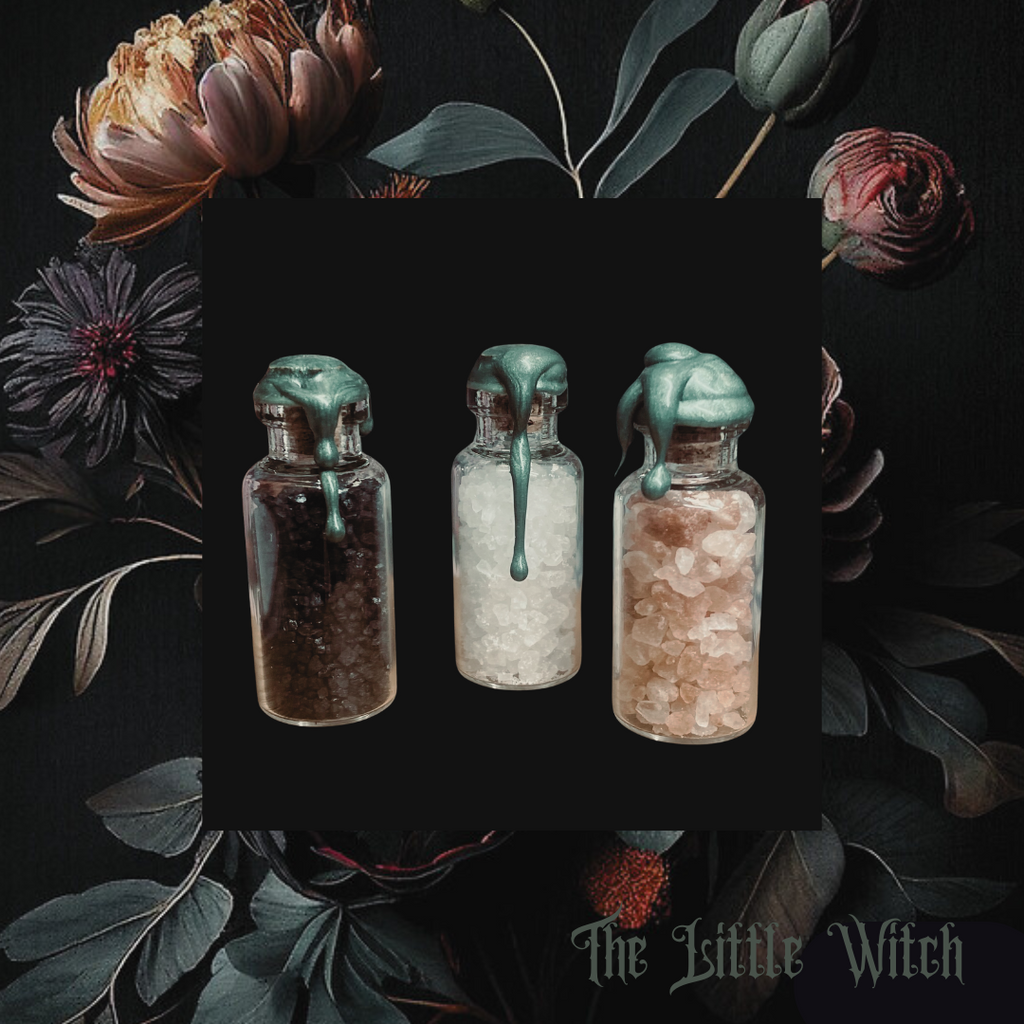 Three small glass jars containing black, white, and pink salts, presented in a floral-themed image with a black drawstring bag labeled 'The Little Witch'.
