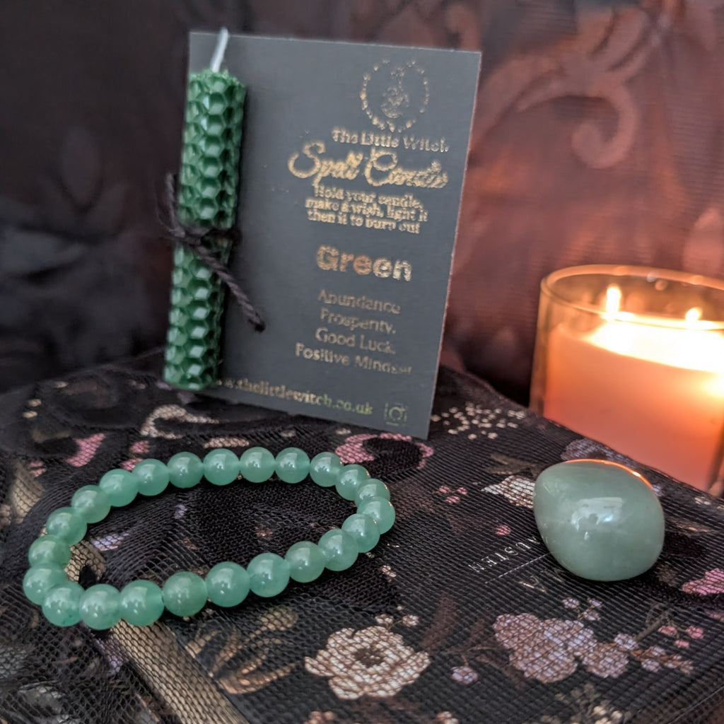Green bracelet, candle, and card on a dark surface with a lit candle in the background