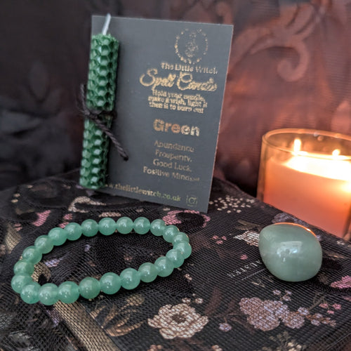 Green bracelet, candle, and card on a dark surface with a lit candle in the background