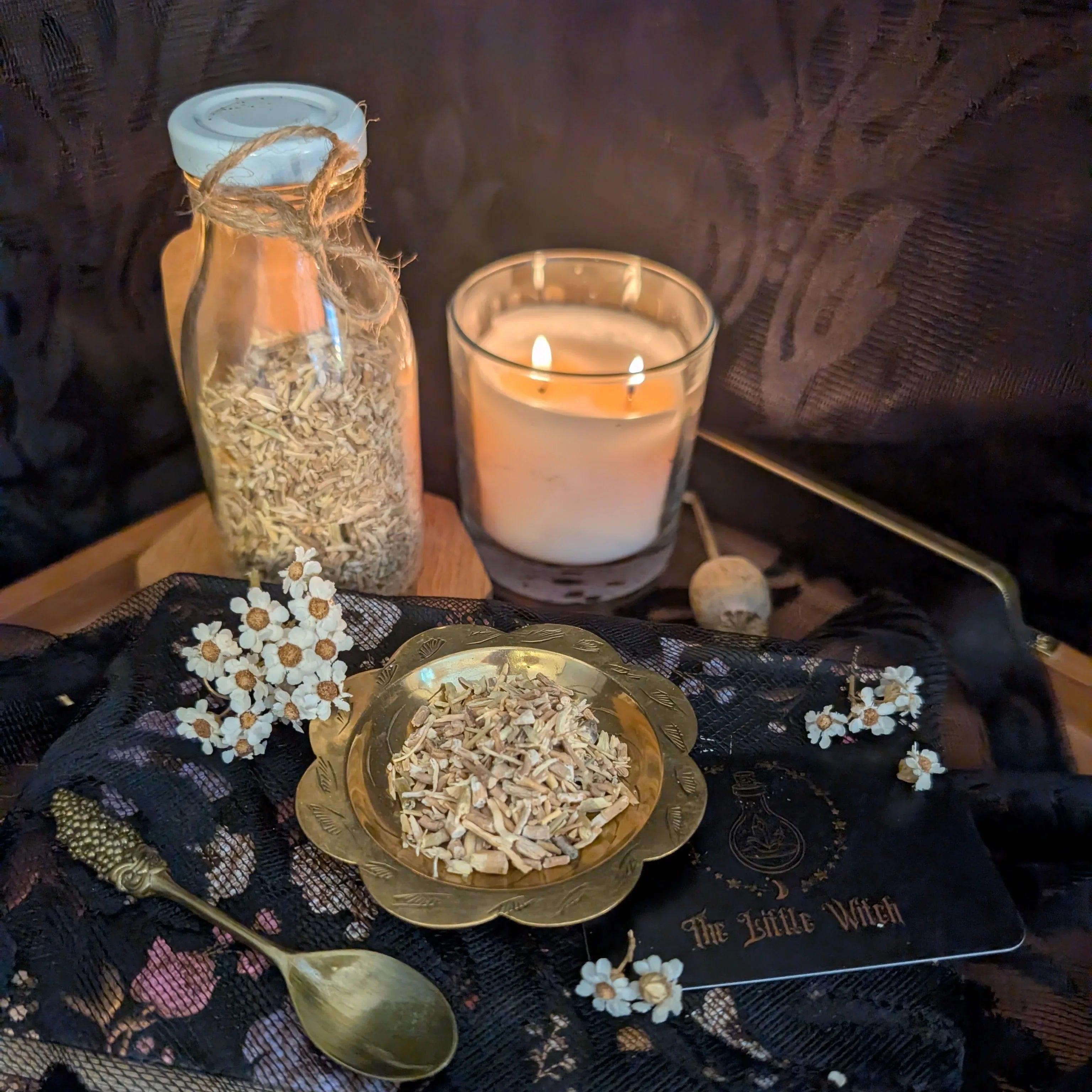 Spells and rituals setup with a candle, jar, and herbs on a dark fabric.