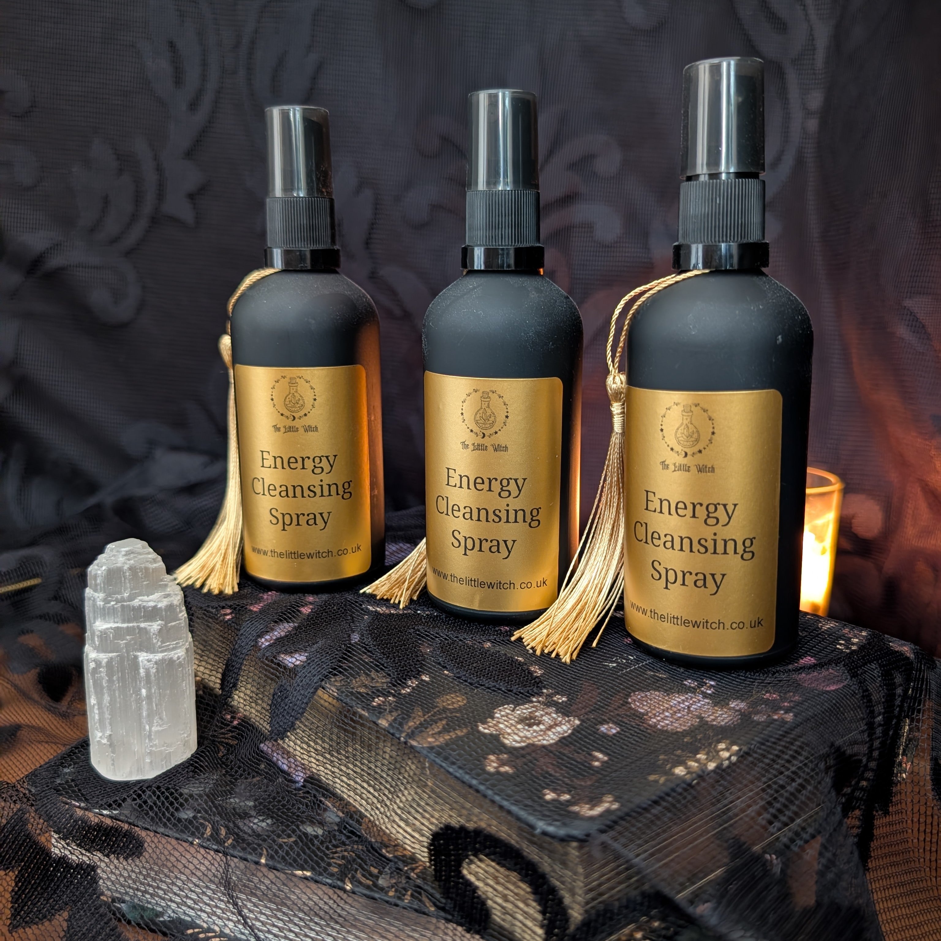 Three bottles of 'Energy Cleansing Spray' on a dark surface with a candle and crystal.