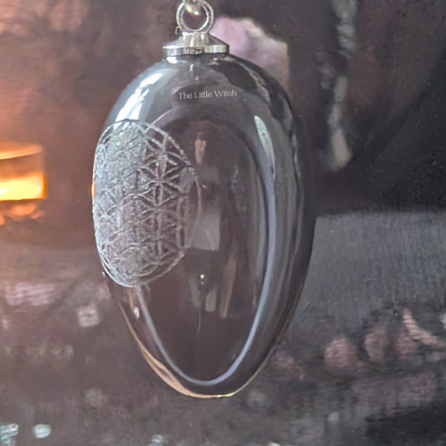 Black obsidian egg pendulum with intricate design and 'The Little Witch' branding.