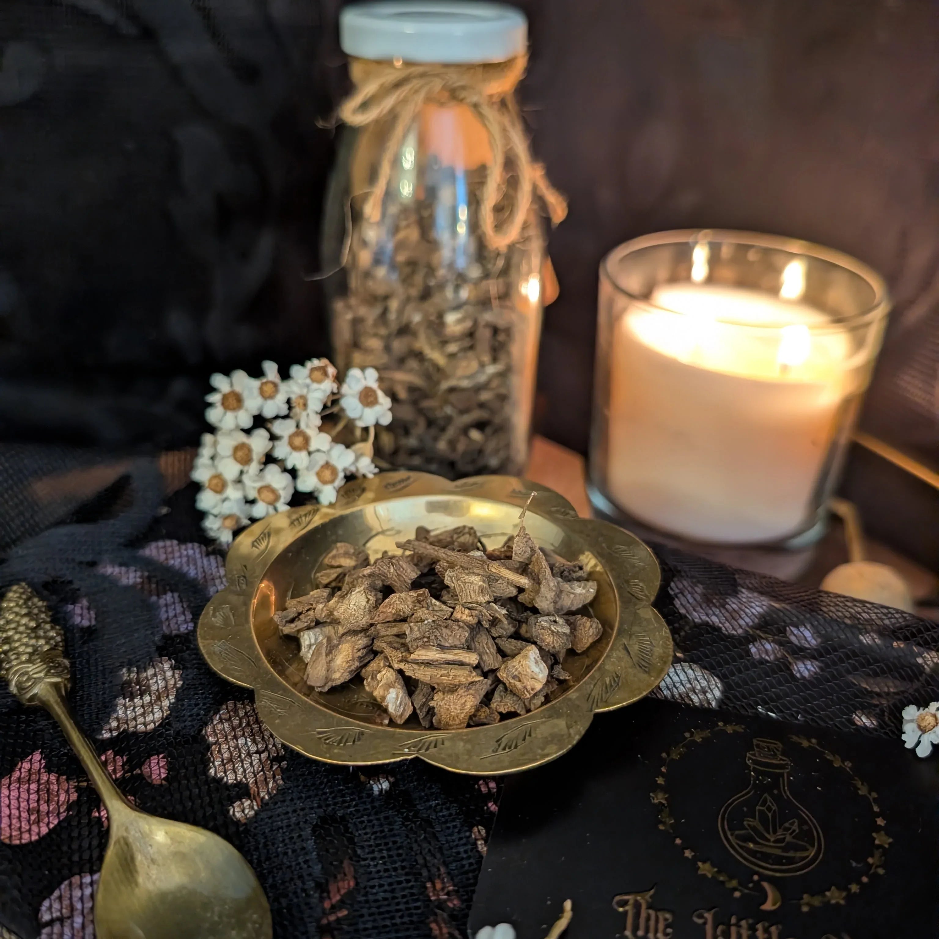Spices in a bowl with a lit candle and jar in the background on a dark surface.