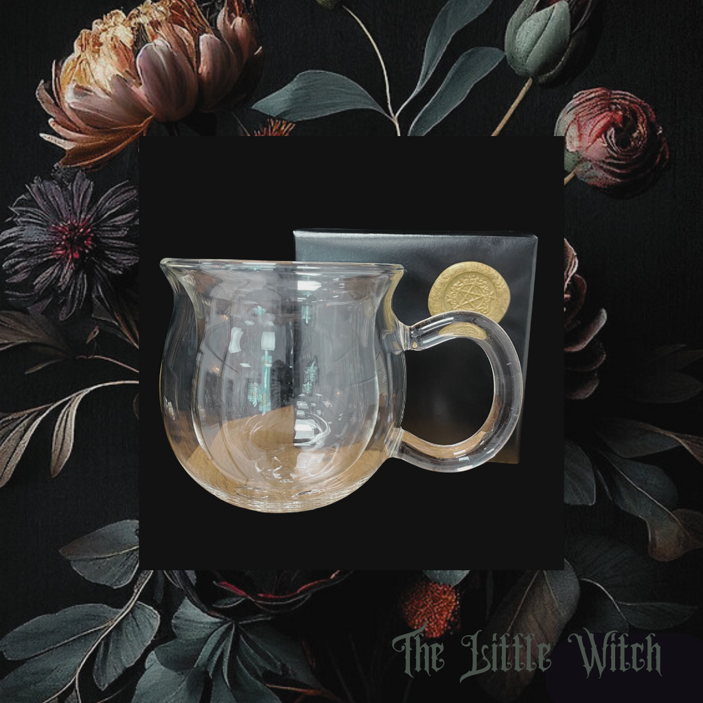 A clear, double walled cauldron-shaped mug with insulation, presented on a dark background with floral elements. The mug has a handle and is made of glass
