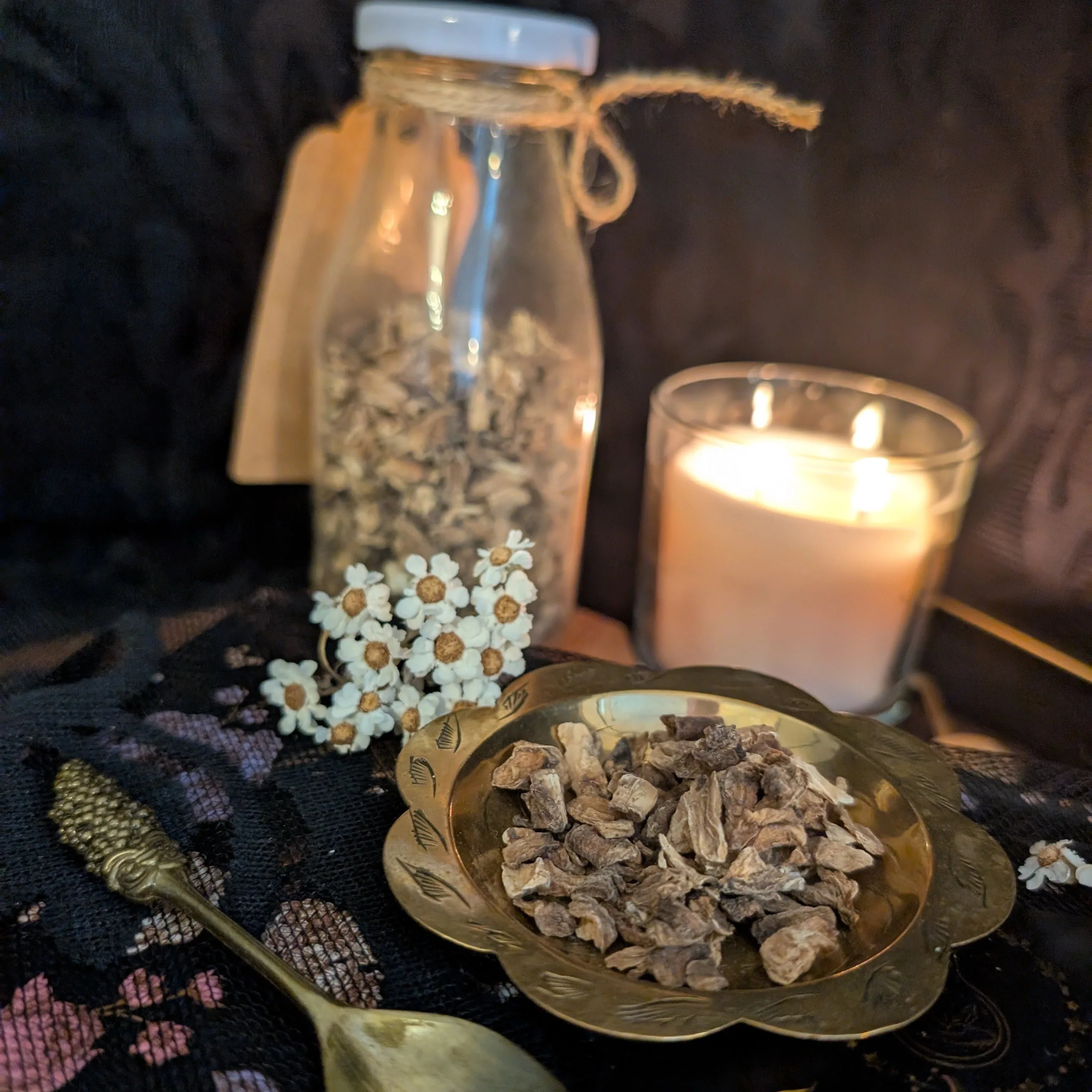 Spices in a bowl with a lit candle and bottle in the background on a dark surface.