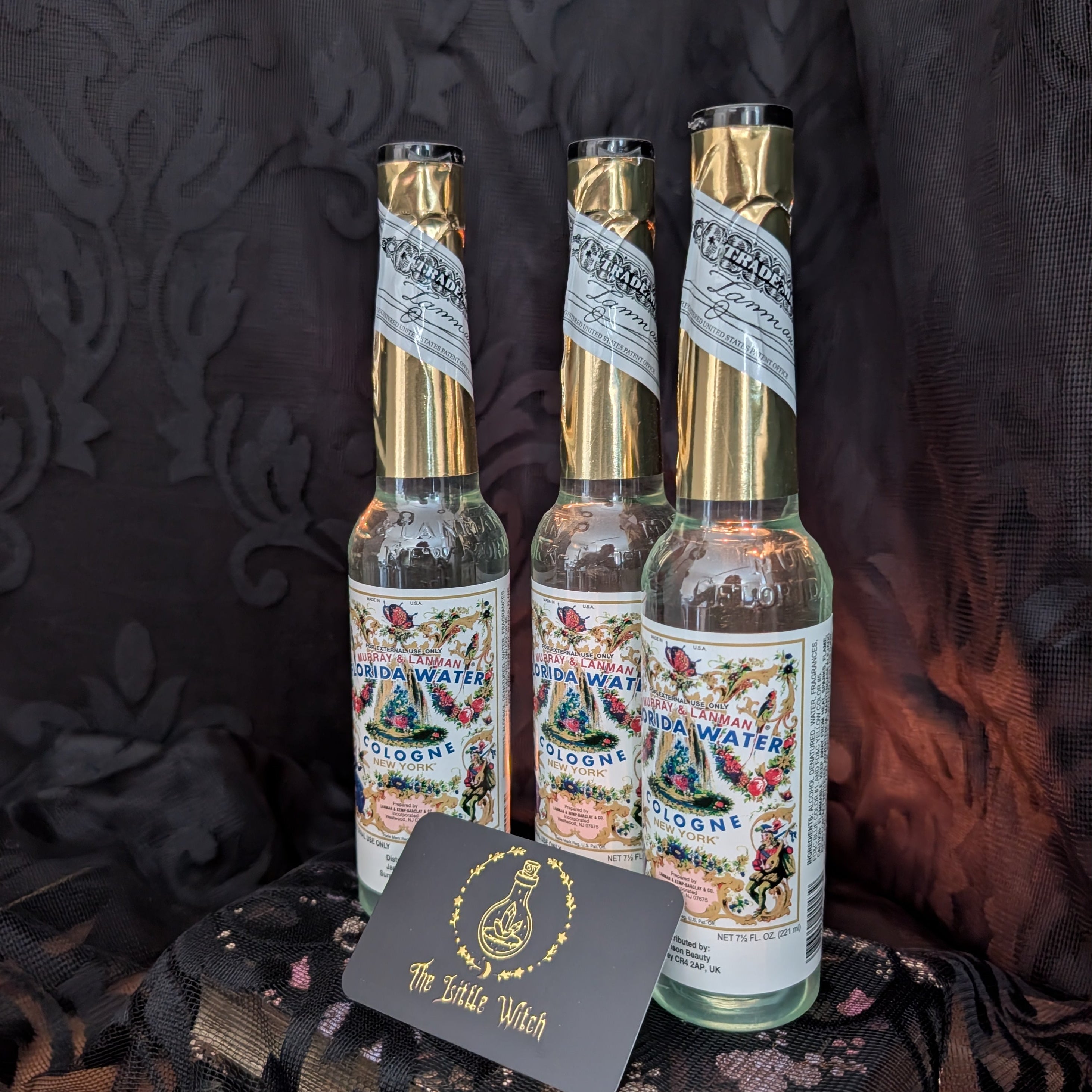Three bottles of  Florida Water on a dark surface with a decorative background