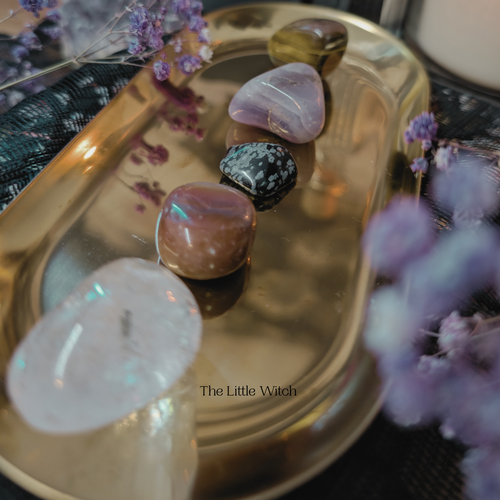 Polished stones on a gold tray with purple flowers.