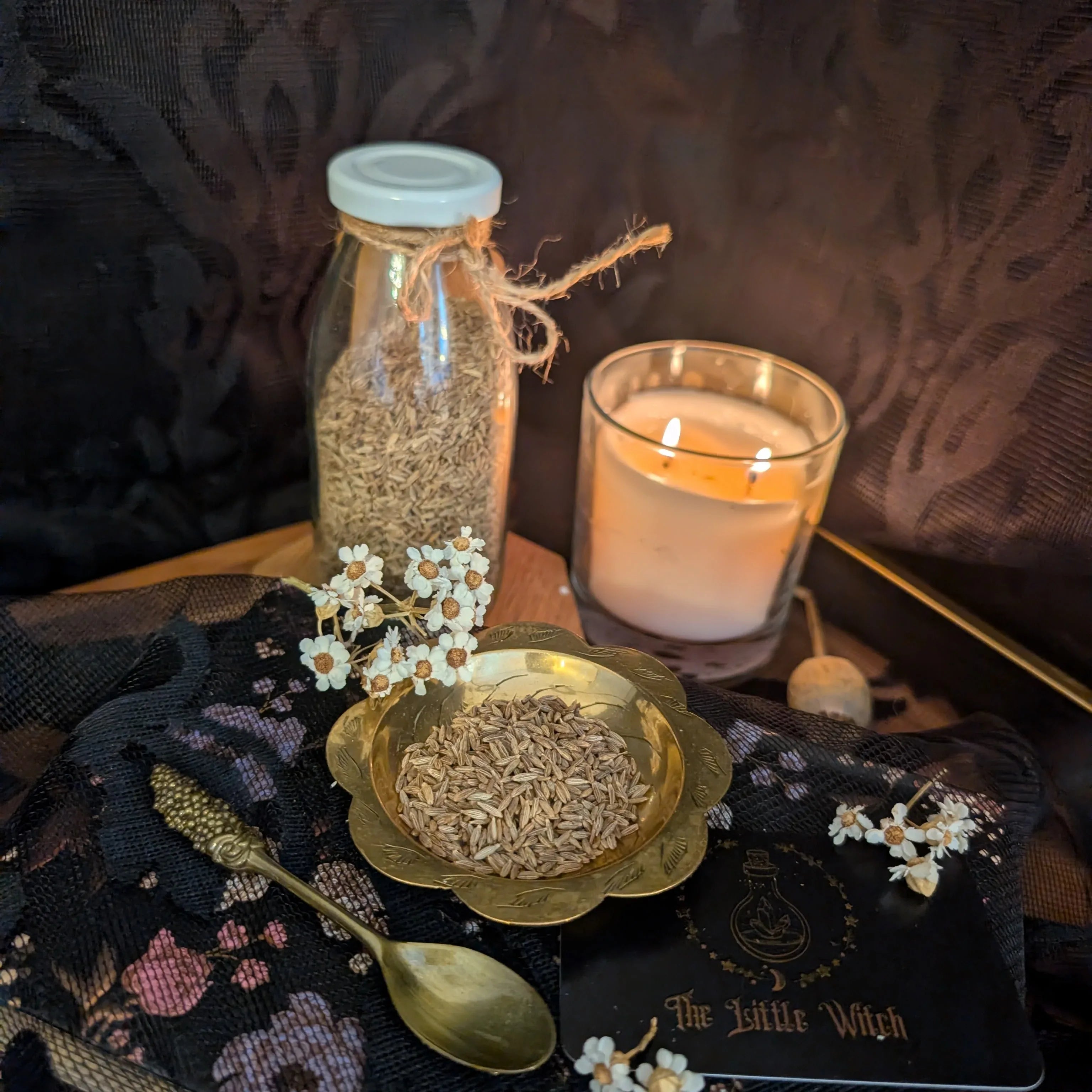 Spices in a jar and bowl with a lit candle on a dark surface