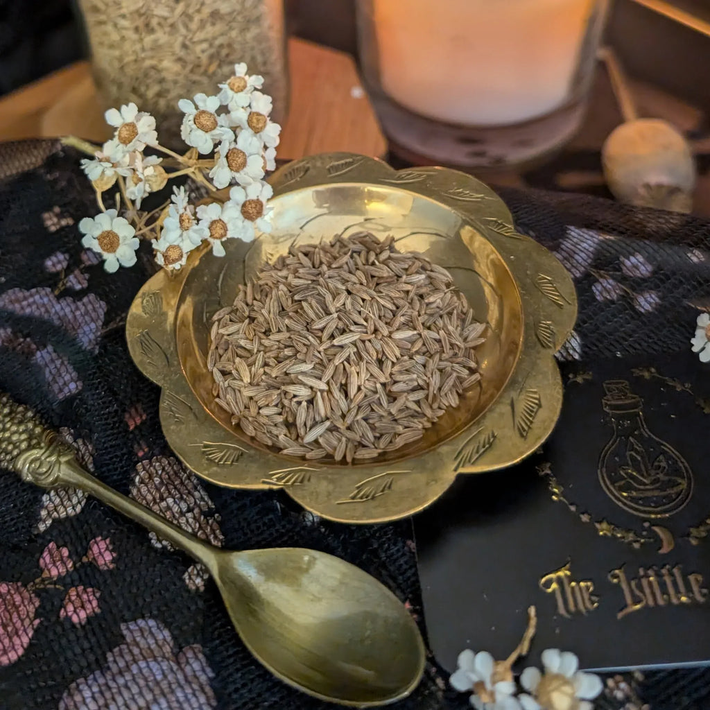 Gold bowl with dried herbs on a decorative surface with flowers and a candle.