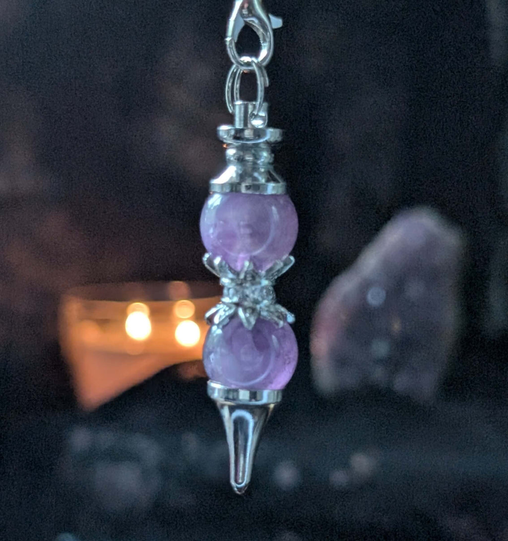 Purple crystal pendulum with silver accents on a dark background