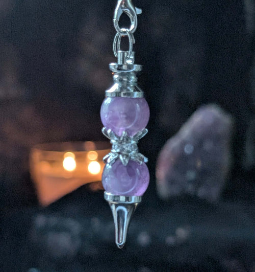 Purple crystal pendulum with silver accents on a dark background