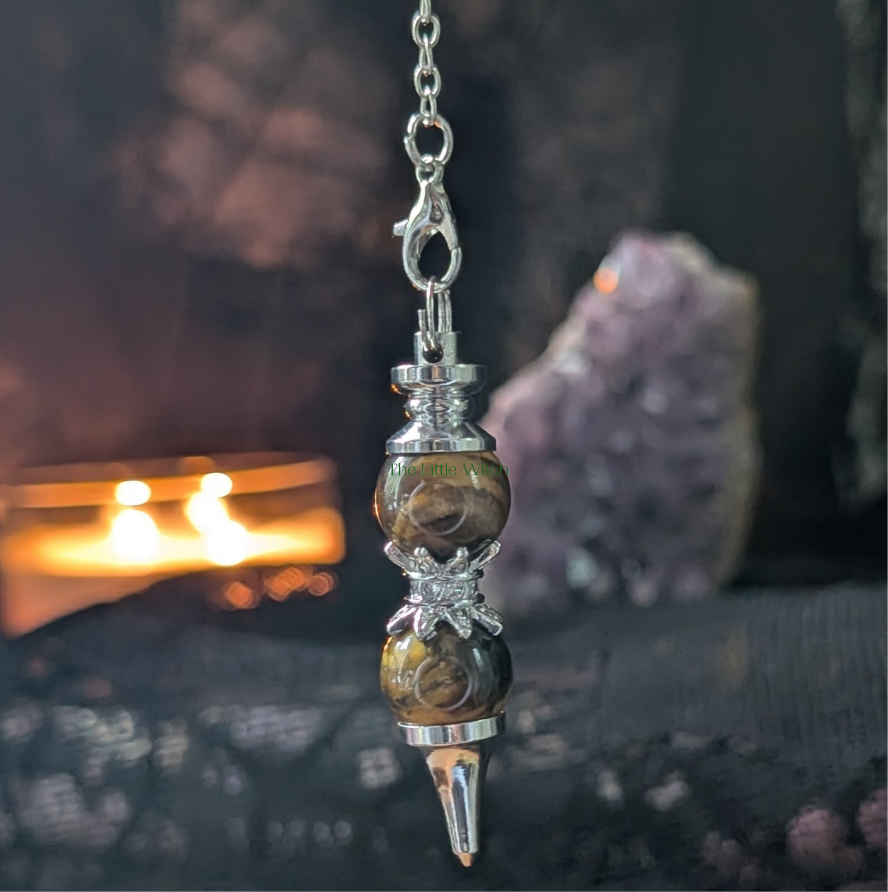 Double Tiger Eye pendulum with black lace backdrop and a softly lit candle and amethyst geode in the background 