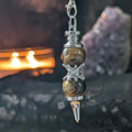 Double tiger eye pendulum with black lace backdrop with a lit candle and amethyst geode in the background 