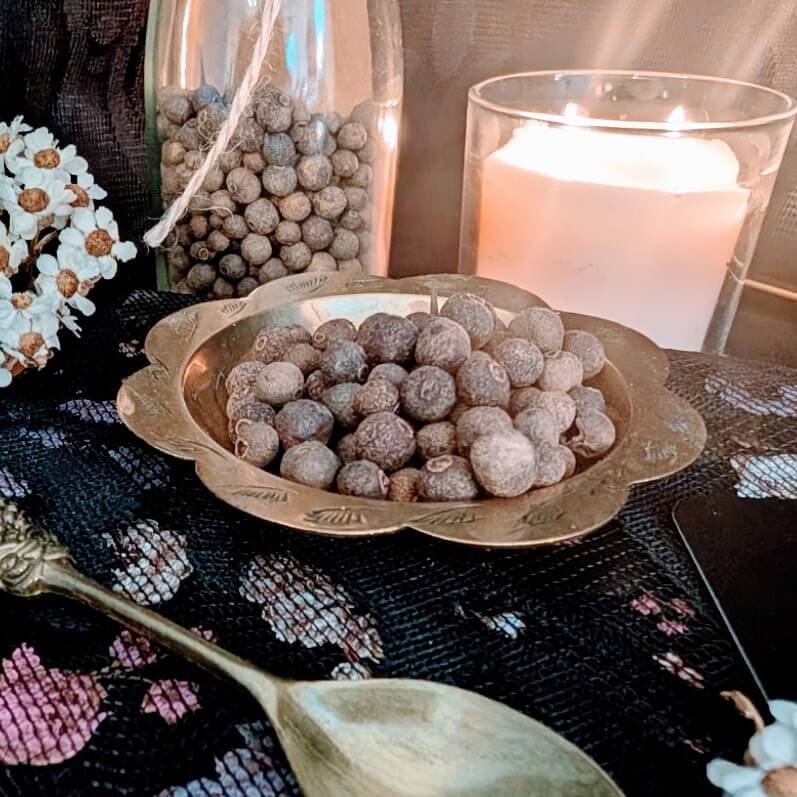 Decorative bowl with Allspice on a table with a candle and flowers.