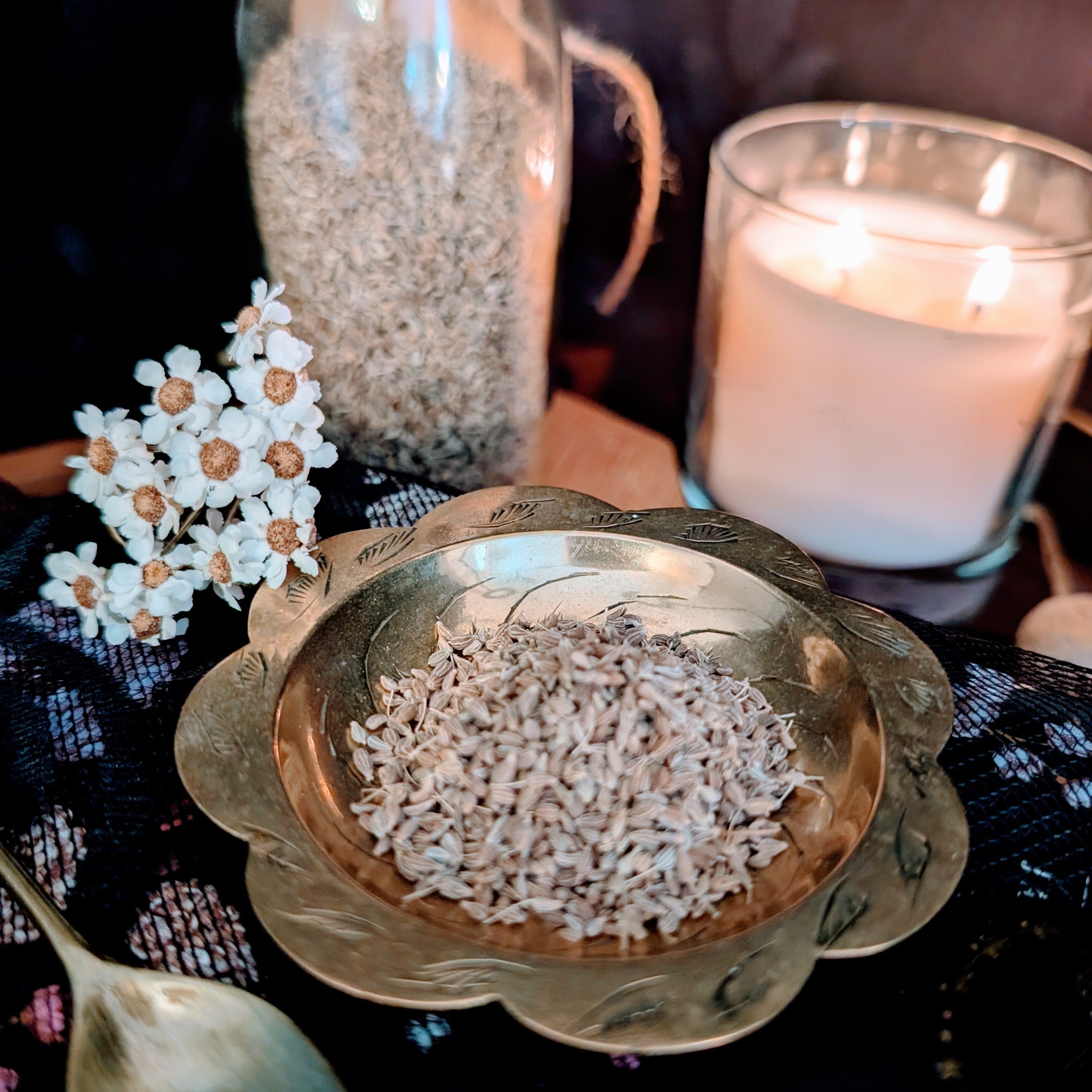Decorative bowl with dried aniseed, white flowers, and a lit candle on a dark surface.
