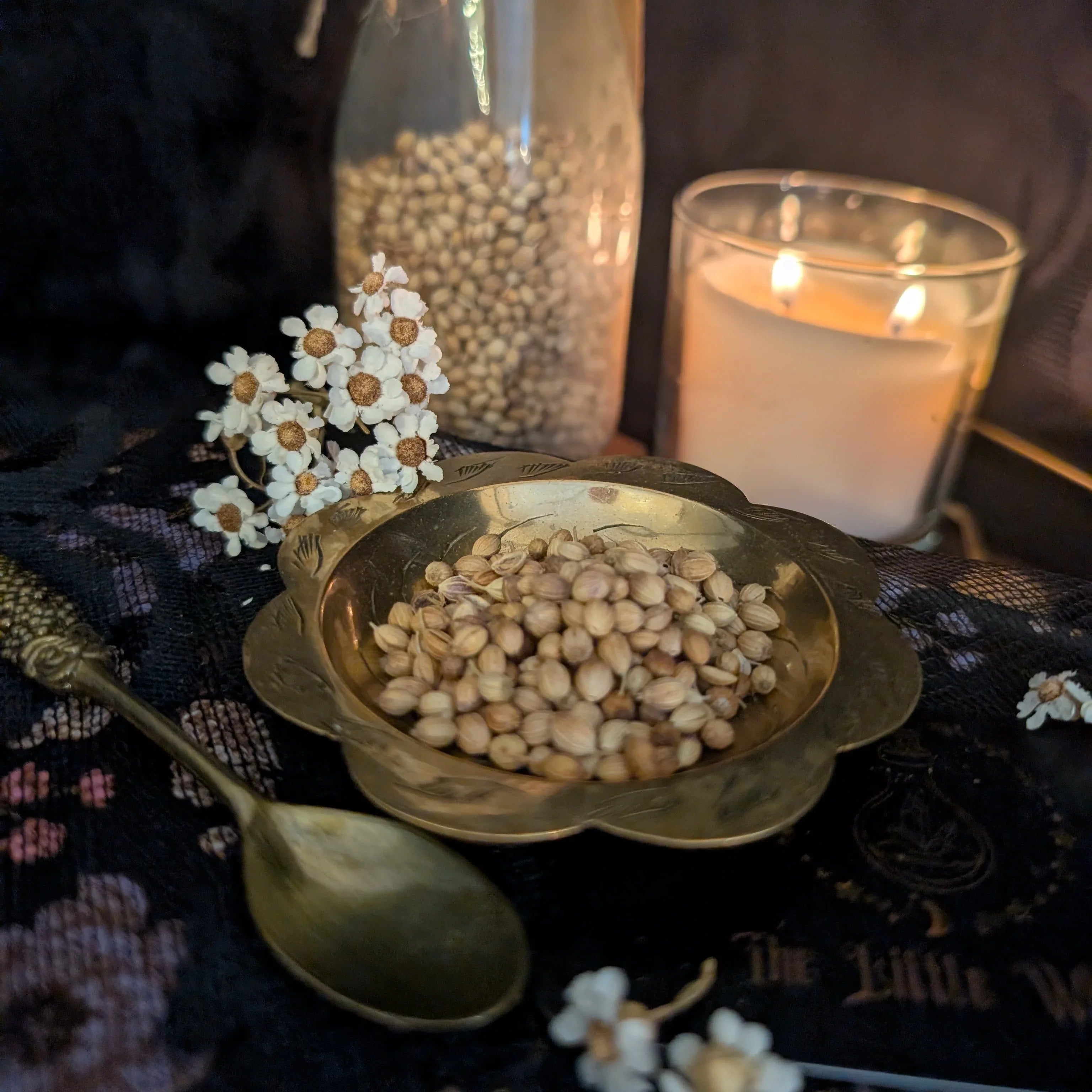 Bowl of coriander seeds with a candle and flowers on a dark surface