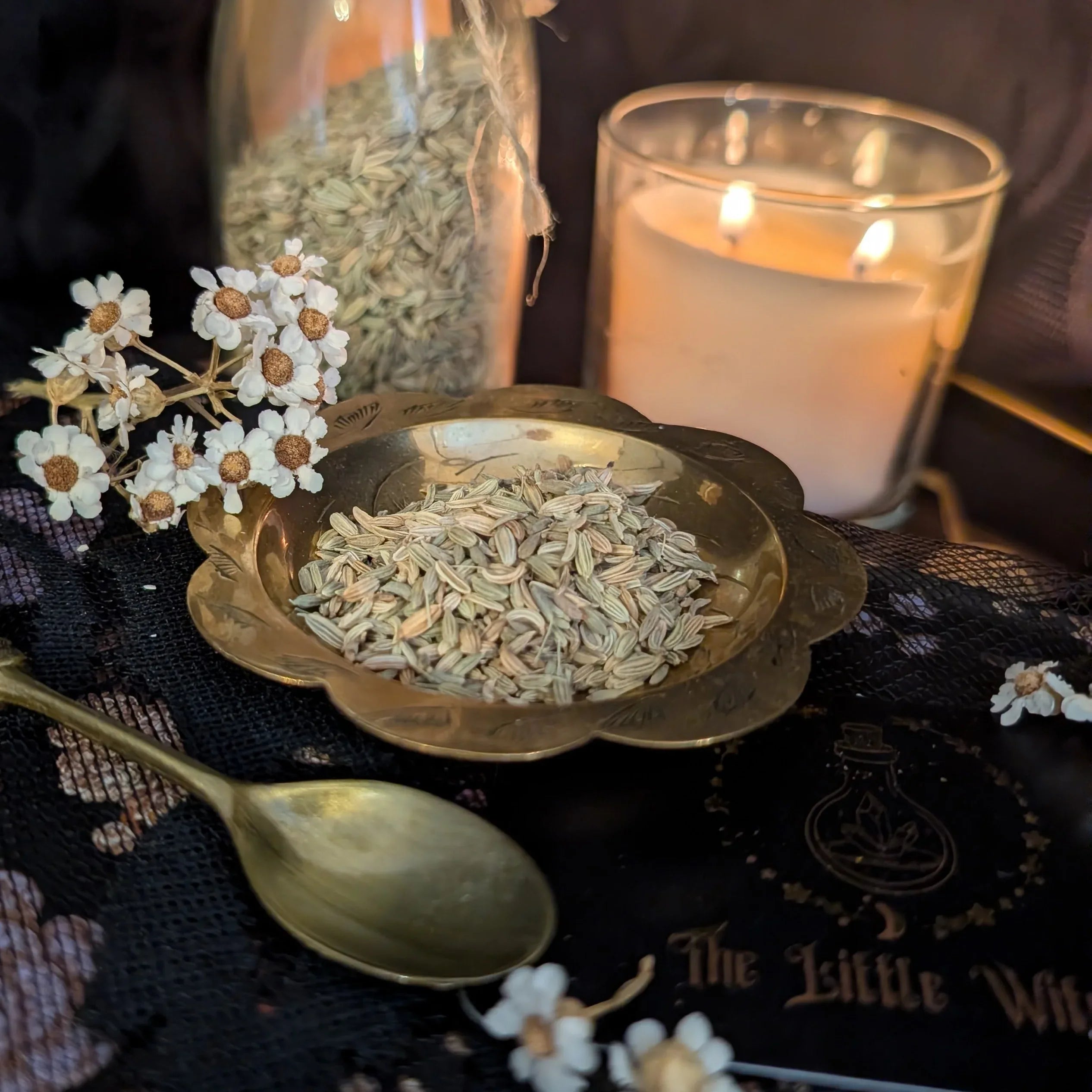 Herbal ingredients in a bowl with a candle and spoon on a dark surface